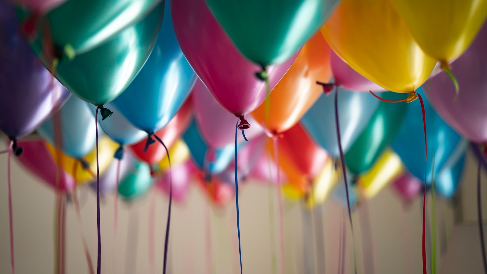 Colourful celebration balloons filling the ceiling at a private milestone event, photographed from below