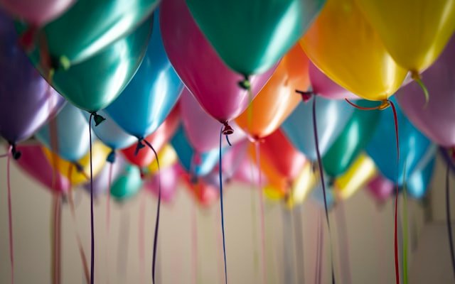 Colourful celebration balloons filling the ceiling at a private milestone event, photographed from below