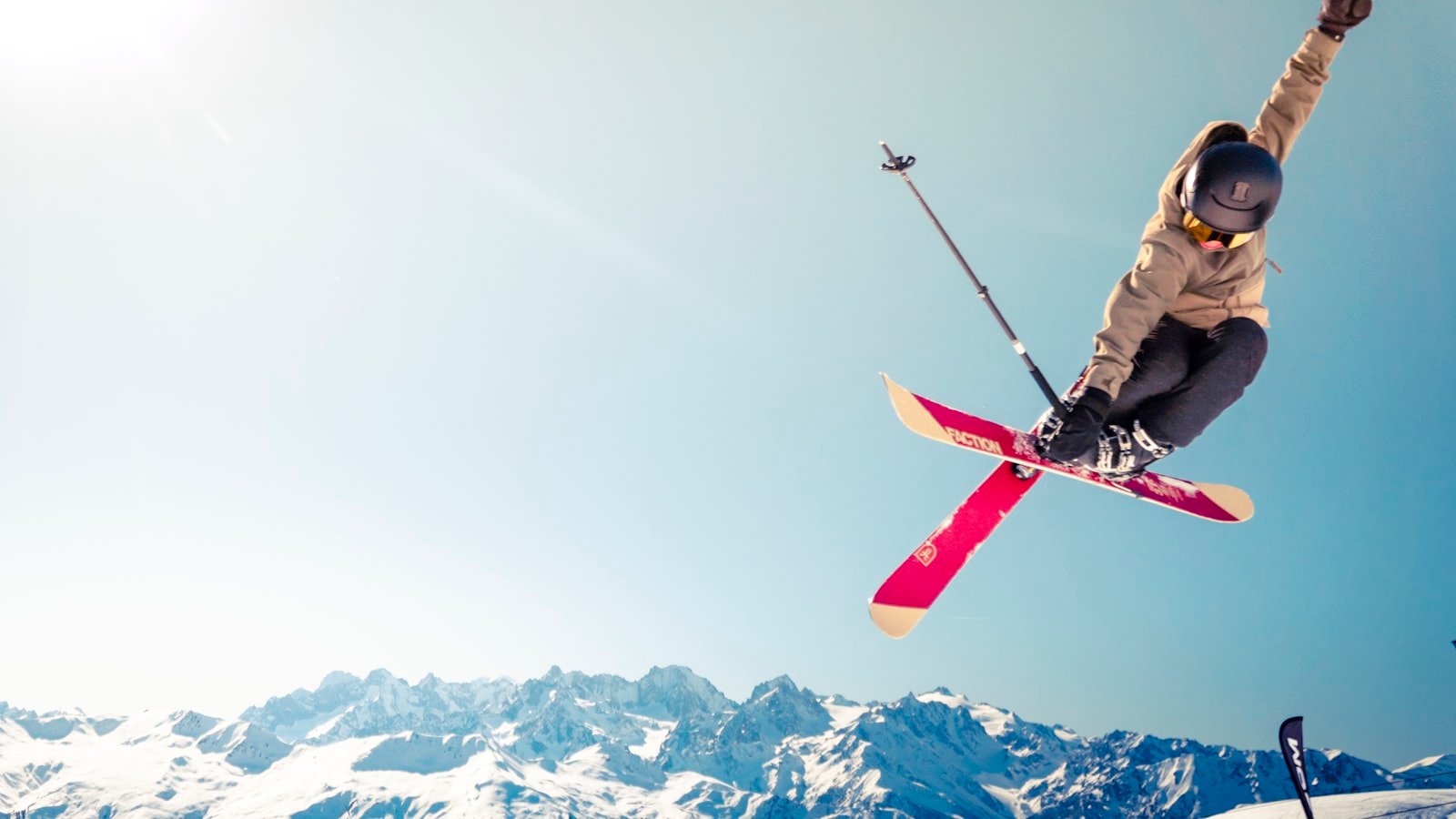 A skier performing an aerial jump against snow-covered alpine peaks, illustrating a guide to a fully handled ski season in Courchevel, Verbier, St Moritz and Gstaad