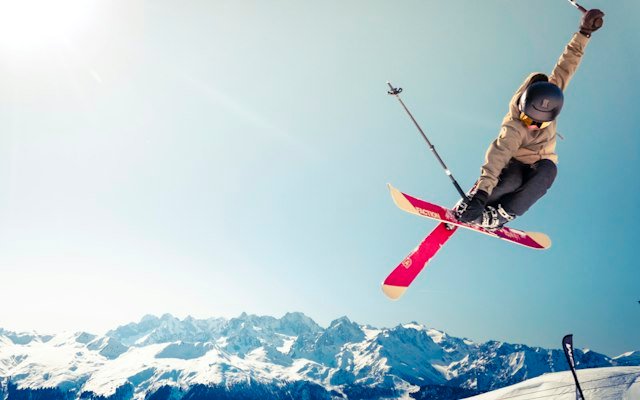 Skier jumping in mid-air over an alpine mountain landscape in the kind of fully handled ski season Algoz arranges in Courchevel, Verbier, St Moritz and Gstaad
