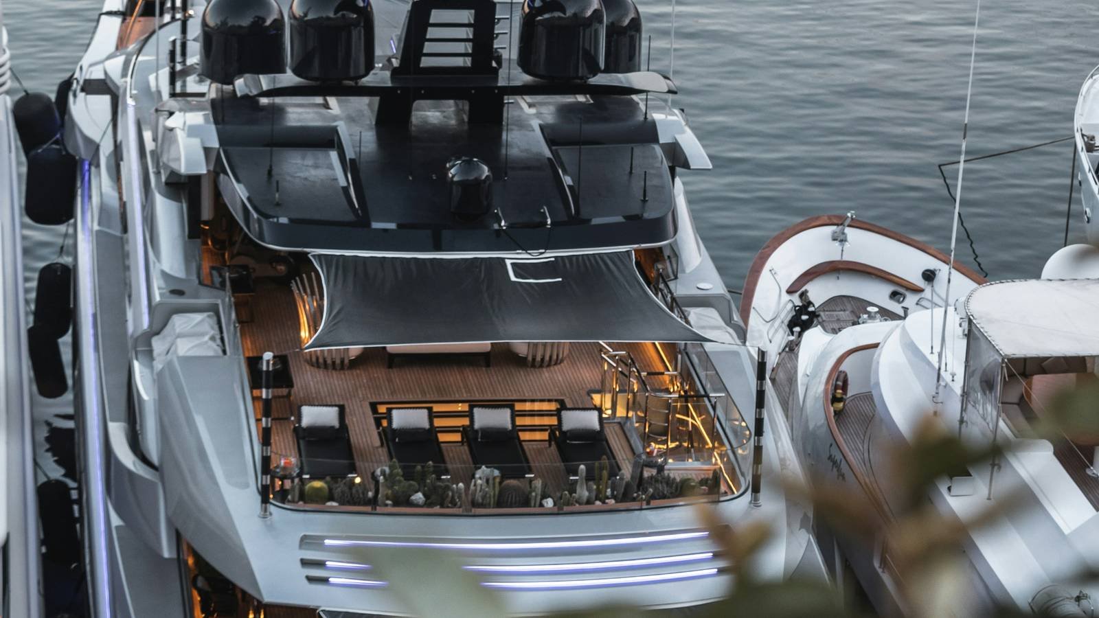 A superyacht moored at dusk with its aft deck lit, seen from above