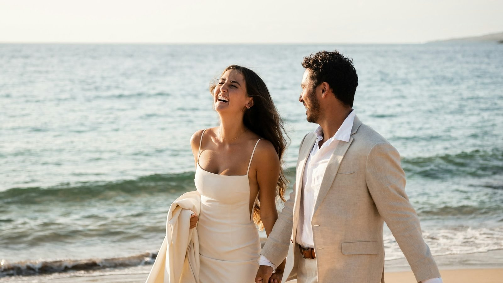 Newlyweds walking hand in hand along a beach at sunset after a destination wedding ceremony